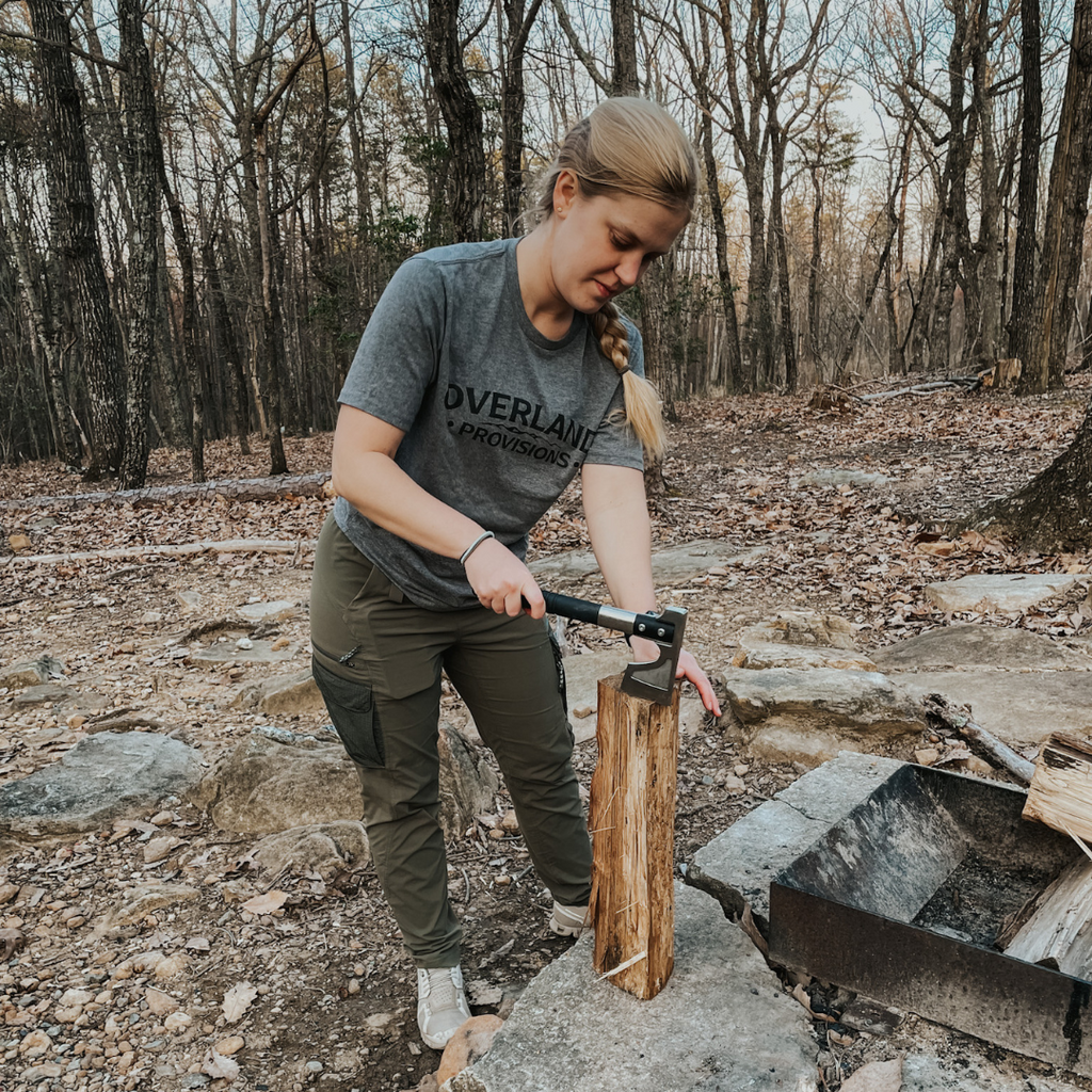 Girl chopping firewood with hatchet, wearing heather gray Overland Provisions t-shirt